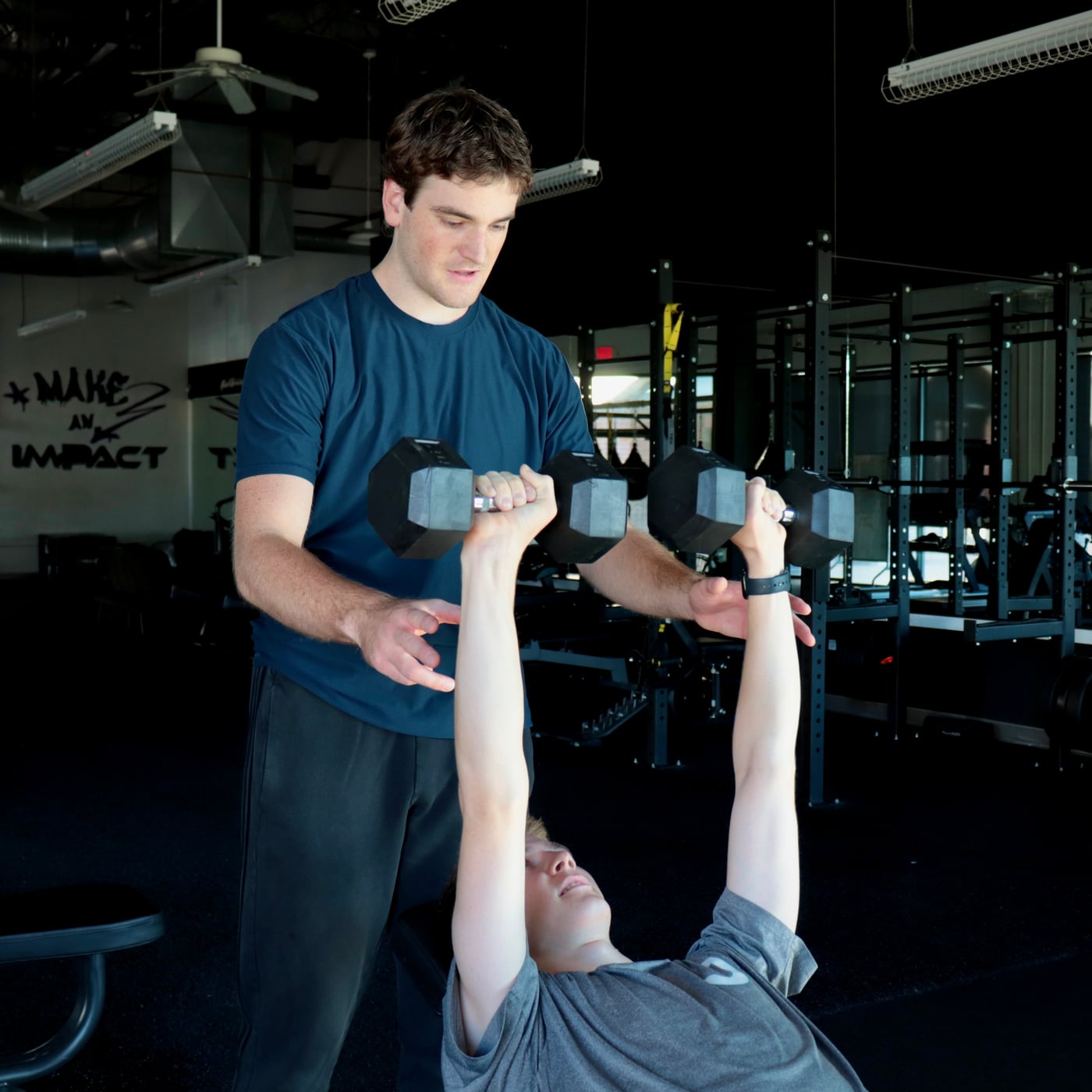 Coach supporting a dumbbell press in the gym